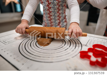 A child rolls out soft dough with a wooden pin, making festive cookies in a warm, joyful holiday kitchen A child rolls out soft dough with a wooden pin, making festive cookies in a warm, joyful holiday kitchen 131307539