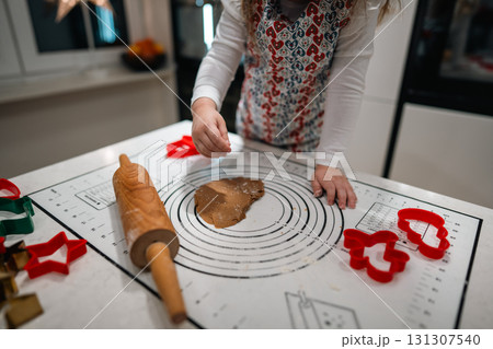 A delighted child bakes cookies with a rolling pin and colorful cutters in a warm, festive holiday kitchen A delighted child bakes cookies with a rolling pin and colorful cutters in a warm, festive holiday kitchen 131307540