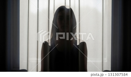 Silhouette of a woman sitting behind a curtain. 131307584