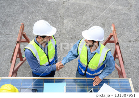 Top view of professional engineering people wearing helmets and safety vests meeting with solar photovoltaic panels handshake for agreement project. green alternative energy concept. Top view of professional engineering people wearing helmets and safety vests meeting with solar photovoltaic panels handshake for agreement project. green alternative energy concept. 131307951