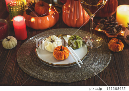 Thanksgiving table setting with decorative pumpkins, candles and string lights on dark wooden table Thanksgiving table setting with decorative pumpkins, candles and string lights on dark wooden table 131308485