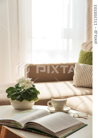 Cozy Living Room with Coffee, Book and African Violet on Table Cozy Living Room with Coffee, Book and African Violet on Table 131308503