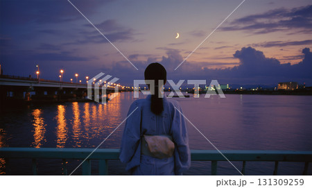 女性が浴衣で薄暮の月と雲の空を河川敷で見上げる 女性が浴衣で薄暮の月と雲の空を河川敷で見上げる 131309259