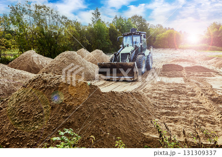 Wheeled excavator spreading sand across playground area, evenly distributing material to prepare smooth surface for construction. Wheeled excavator spreading sand across playground area, evenly distributing material to prepare smooth surface for construction. 131309337