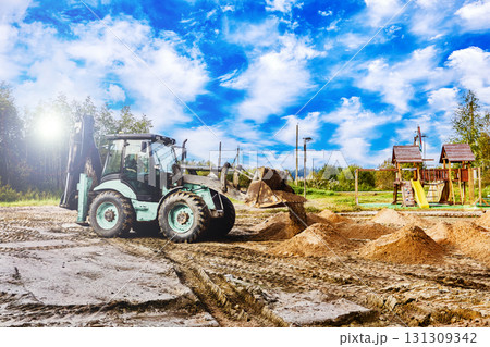 Digger is located on sandy site with bucket raised near high sand pile, several other piles are arranged across ground surface of working area. 131309342