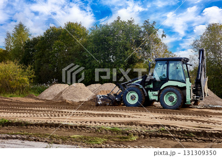 Front end loader performs finish grading by precisely redistributing loose sand layer and removing minor surface irregularities for optimal site compaction. Front end loader performs finish grading by precisely redistributing loose sand layer and removing minor surface irregularities for optimal site compaction. 131309350
