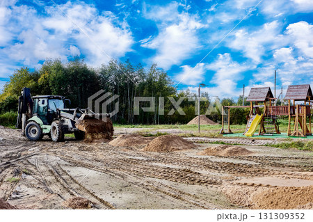 Loader pushes piles of sand across a flat construction site near wooden playground structures. Loader pushes piles of sand across a flat construction site near wooden playground structures. 131309352