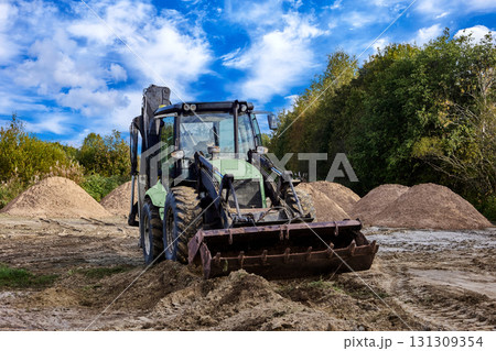 Wheel loader performs earthmoving work with sand piles visible on construction site. Wheel loader performs earthmoving work with sand piles visible on construction site. 131309354