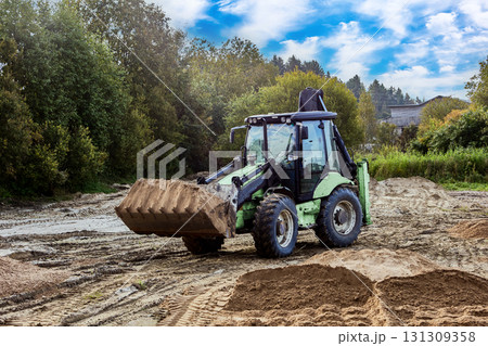 Wheel mounted earthmover spreads material on work area, preparing base for upcoming construction tasks. 131309358