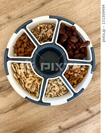 A plate filled with nuts, walnuts, cashews, dried bananas, and dates. A plate with dried fruits and nuts sits on the table. 131309494