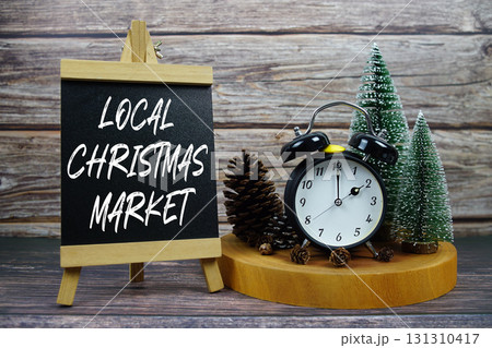 Local Christmas Market written on easel with vintage alarm clock, pinecones, and miniature Christmas trees Local Christmas Market written on easel with vintage alarm clock, pinecones, and miniature Christmas trees 131310417