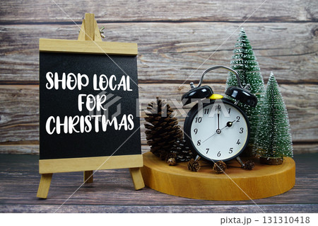 Shop Local For Christmas written on easel with vintage alarm clock, pinecones, and miniature Christmas trees Shop Local For Christmas written on easel with vintage alarm clock, pinecones, and miniature Christmas trees 131310418