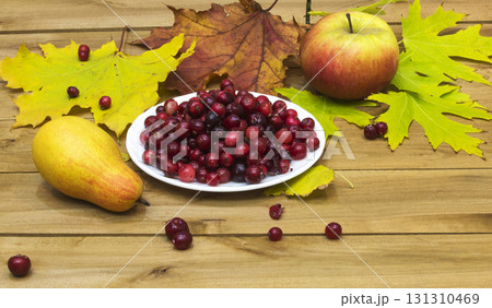 Autumn Still Life. Cranberries on a white plate, autumn leaves and an apple with a pear 131310469