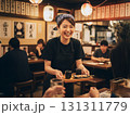 焼き鳥を運ぶ明るい居酒屋の女性スタッフ：賑わう店内の活気 131311779