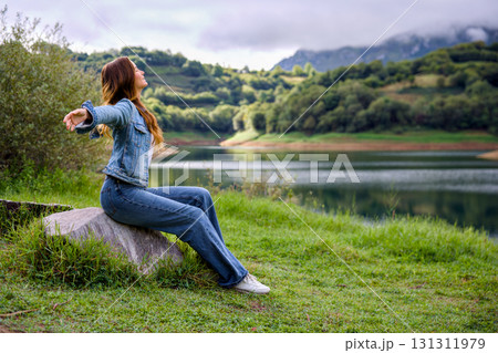 Woman stretching arms sitting by mountain lake outdoors Woman stretching arms sitting by mountain lake outdoors 131311979