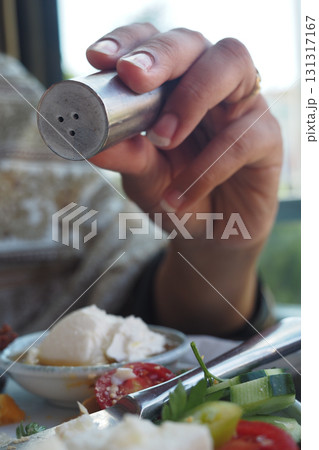 Hand holding a salt shaker over a plate of food 131317167