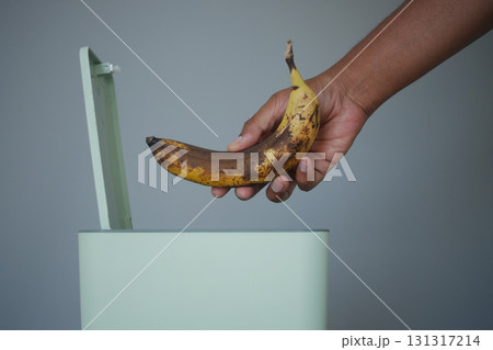 Hand discarding a ripe banana into a trash bin 131317214