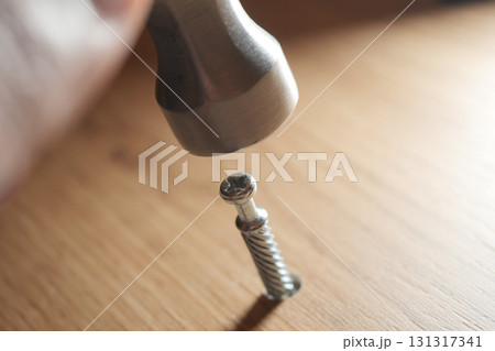 Hammer striking metal screw on wooden surface Hammer striking metal screw on wooden surface 131317341