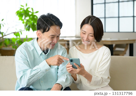 ソファに座ってスマホを見る男女 131317796