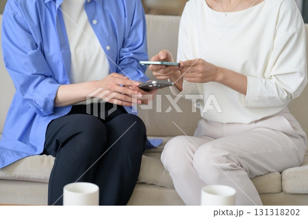 並んでソファに座ってスマホを見る女性 131318202
