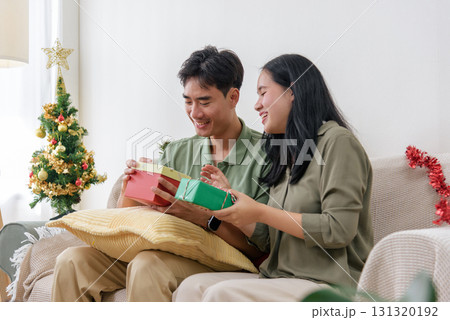 Christmas holiday finds happy couple sharing love and presents at home during winter, enjoying festive day opening colorful gifts near decorated tree, warm christmas celebration. 131320192