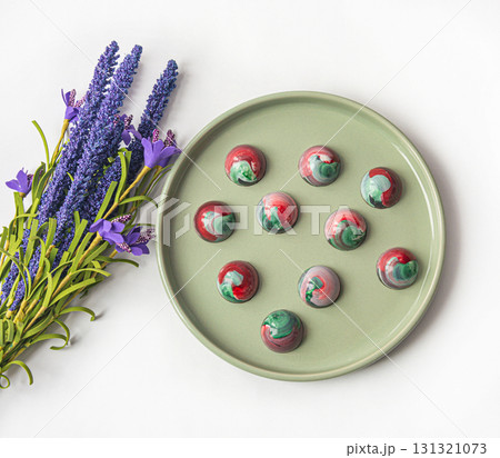 Collectible handmade tempered chocolate sweets with a glossy painted body on a round plate with blur elements. View from above 131321073