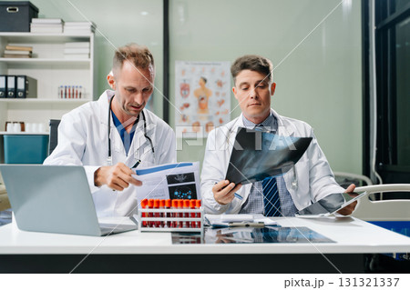Doctors analyzing an X-ray, collaborating with digital tools in a medical office. Showcasing teamwork, diagnostic Doctors analyzing an X-ray, collaborating with digital tools in a medical office. Showcasing teamwork, diagnostic 131321337