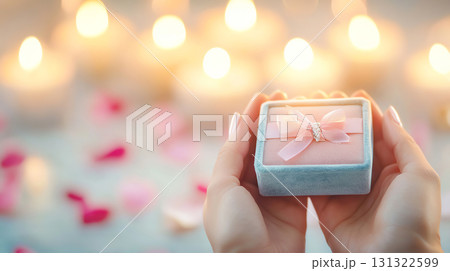 person holds small velvet jewelry box with ribbon, surrounded by candles 131322599