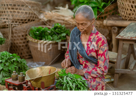 An Elderly Woman Engaged in the Preparation of Fresh Green Vegetables Within a Market Setting An Elderly Woman Engaged in the Preparation of Fresh Green Vegetables Within a Market Setting 131325477