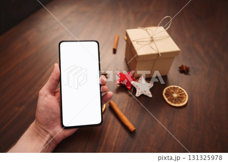 Man hand hold smarthone with white screen with christmas decorations on background Man hand hold smarthone with white screen with christmas decorations on background 131325978