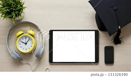 Overhead view of a tablet, smartphone, earphones, and graduation cap on wood, highlighting themes of digital learning and education 131326390