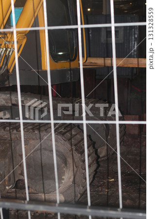 An excavator is behind a safety fence at a construction site for protection and security An excavator is behind a safety fence at a construction site for protection and security 131328559
