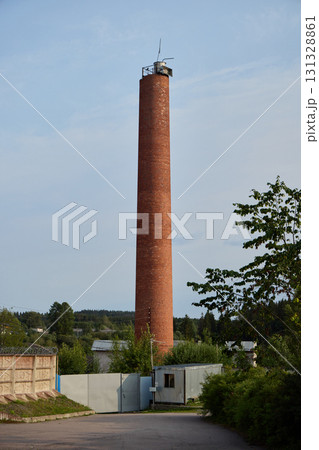 A striking industrial red brick chimney stands tall against the clear blue sky during daylight 131328861