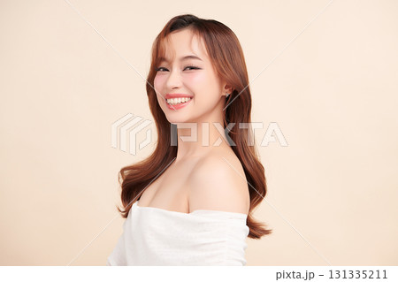 A beautiful young Asian woman with clean, fresh skin against a beige background. Skincare, facial treatment, cosmetology, beauty, and spa. An elegant portrait of an Asian woman. 131335211