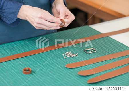 A woman attaches accessories to a leather belt. Leatherworker's workshop.  131335344
