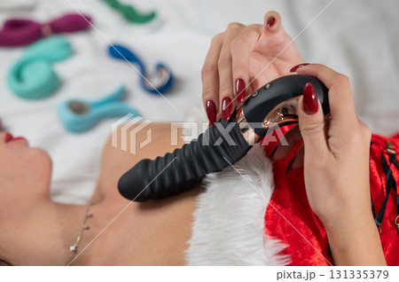 Caucasian woman in Santa Claus costume lying on bed and holding dildo. Sex toys collection.  131335379