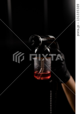Close-up of instant tanning equipment in the hands of a master. Gun spraying paint for leather against black background Close-up of instant tanning equipment in the hands of a master. Gun spraying paint for leather against black background 131335389