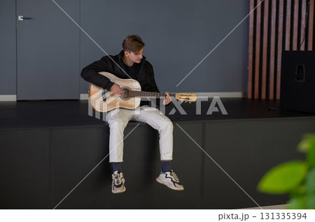 Caucasian man playing guitar while sitting on stage.  131335394