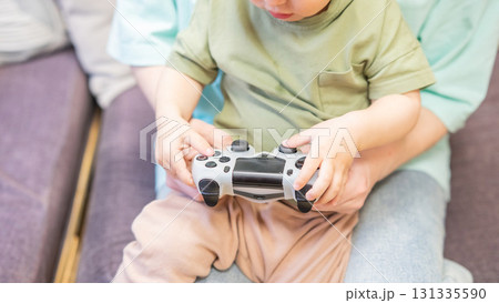 Caucasian woman teaches her little son to play console. Joystick in hands. Caucasian woman teaches her little son to play console. Joystick in hands. 131335590