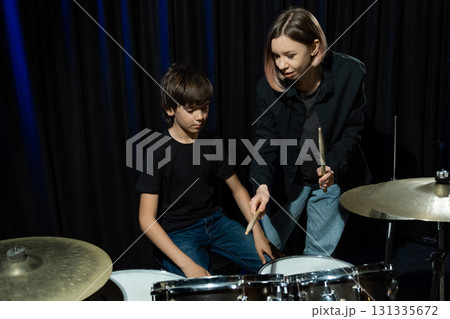 Young caucasian woman teaches a boy to play the drums in the studio on a black background. Music school student Young caucasian woman teaches a boy to play the drums in the studio on a black background. Music school student 131335672