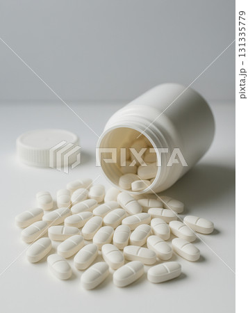 White tablets spilling from an open plastic bottle on a clean white background. Perfect for 131335779