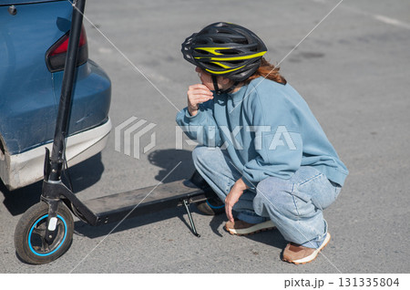 A distressed woman examines the damage after a collision between an electric scooter and a car. 131335804