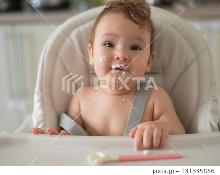 Cute baby boy smeared in sour cream sits in a high chair.  Cute baby boy smeared in sour cream sits in a high chair.  131335886