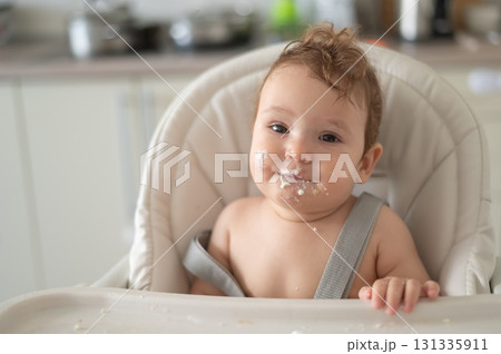 Cute baby boy smeared in sour cream sits in a high chair. Cute baby boy smeared in sour cream sits in a high chair. 131335911