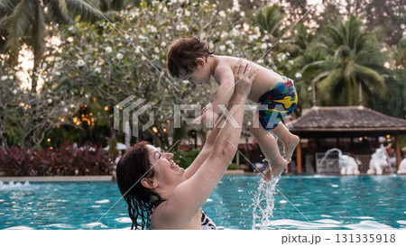 Caucasian woman holds son while swimming in pool on vacation. Caucasian woman holds son while swimming in pool on vacation. 131335918