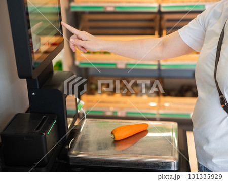 A woman weighs carrots at a self-checkout. A woman weighs carrots at a self-checkout. 131335929