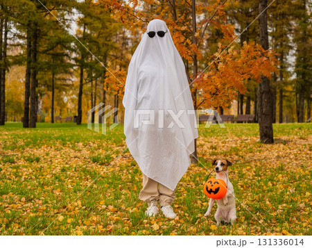 Woman in white sheet and jack russell terrier dog holding jack o latrine in autumn forest. Halloween costume.  131336014