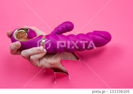 Female hand sticking out with pink sex toy from pink paper background. 131336105
