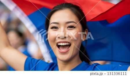 Young Asian woman cheering with a flag at a sports event. Enthusiastic fan celebrating victory. National pride and support concept 131336111