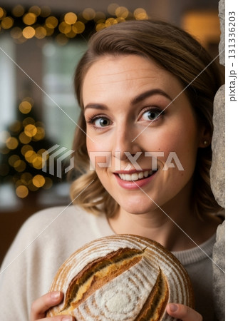 Smiling woman holding a fresh loaf of artisanal sourdough bread. Cozy portrait with a festive Christmas background. Home baking and holiday concept 131336203